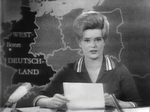 Verwandtenbesuche in Westdeutschland werden für Rentner möglich | Bildquelle: DRA/Screenshot »Aktuelle Kamera« (02.11.1964) Screenshot »Aktuelle Kamera«: Moderatorin sitzt für Karte des geteilten Deutschlands
